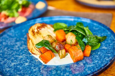 Grilled vegetables (cabbage, carrots, potatoes) with sauce lie on a plate.の写真素材