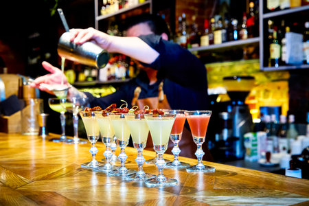 The bartender pours yellow cocktails into shots on a high leg on the bar