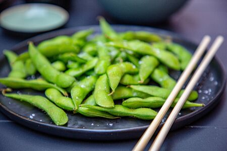 Cooked green Edamame lie on a dark plate in a Japanese restaurant.の写真素材