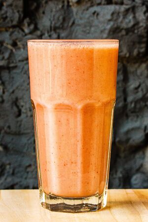 Orange citrus smoothie in a large glass glass against a dark stone wallの写真素材