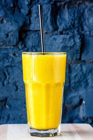 Yellow smoothie (orange, mandarin) in a large glass cup against a dark wall.の写真素材