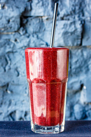 Dark red or Burgundy fruit and berry smoothie in a large glass glass against a dark stone wall