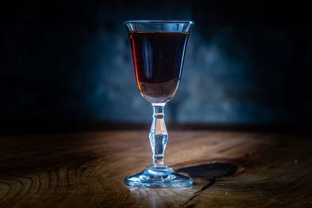 Dark red tincture or liqueur in a glass is on the table in the night bar