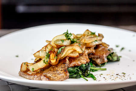 Roast beef liver with spinach and onions on a plateの写真素材