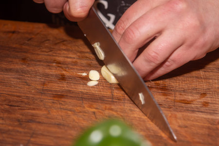 Chef slicing garlic on the cutting board with a knife.