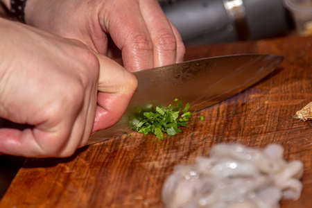 the cook cuts parsley and dill on a wooden board. cooking in a restaurant, chef's hand cutting greens on a wooden board, vegan salad with parsley, vegetable food conceptの写真素材