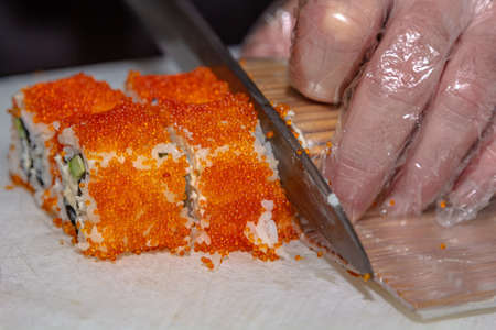 Cook's hands close-up. A male chef makes sushi and rolls from rice, red fish and avocado. white gloves. dark background.の写真素材