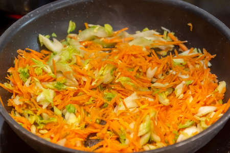 homemade cooking. A woman fries onions and carrots in a hot frying pan with vegetable oil. close-up.の写真素材
