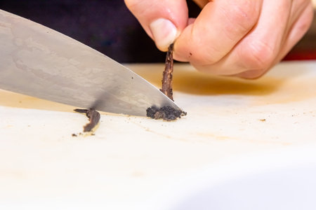 Scratch out vanilla pulp from pod with a knife on a bamboo cutting board.