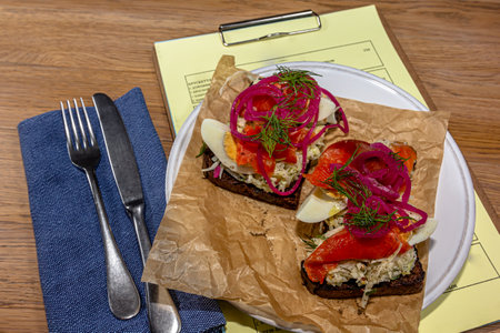 Smorrebrod, an open sandwich with boiled salmon, cream cheese, quail egg and cucumber slices on a white plate on a wooden background. Sandwich recipes. Danish cuisine.の写真素材