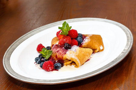 Pancakes with fresh berries on a white plate on a wooden tableの写真素材