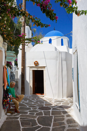 Shop keeper in front of his shop in a treet with a small church in Naousa village on Paros island, Greeceのeditorial素材