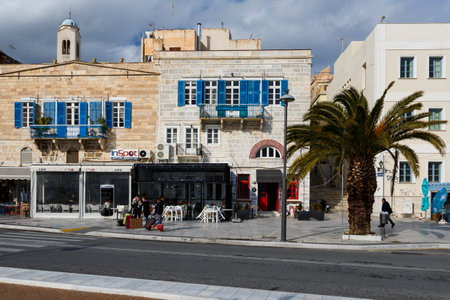 Few people with travel luggage at the seafront of Ermoupoli town on Syros island in Greece.のeditorial素材