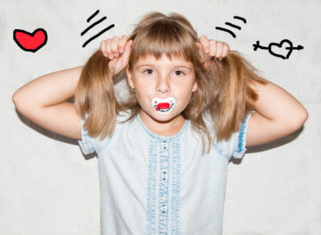 Nice girl with a pacifier in teeth makes hair - hearts aroundの写真素材