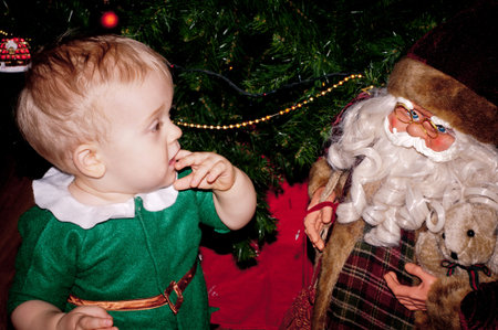 Little baby biy sits under decorated Christmas tree with Santa