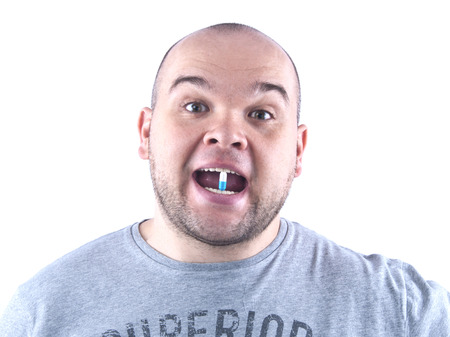 Young bald man in a T-shirt with a tablet in the mouth isolated whiteの写真素材