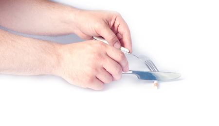 Fork and knife in a man's hands. Cigarette cut with a knife on a white background. Stop smoking.の写真素材