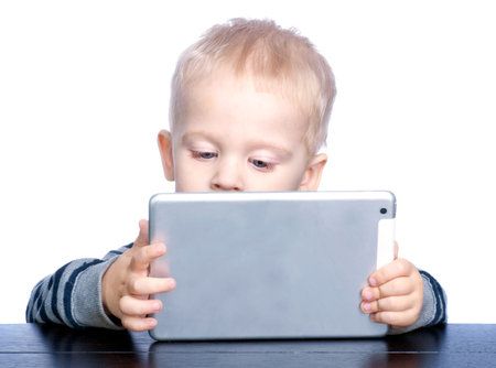 Beautiful little boy with blond hair and blue eyes is holding a tablet. Boy portrait.