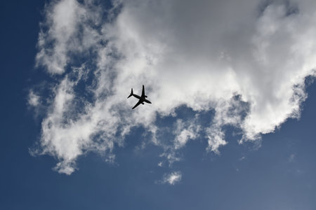 Silhouette of a transport plane flying in a blue sky with a cloud in the background
