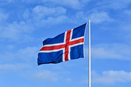Icelandic flag waving in the wind against a blue sky with clouds