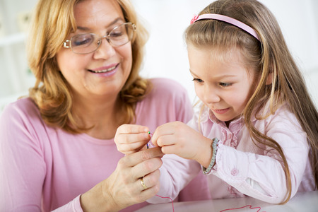 Young cute little girl making bead Jewelry with Grandmother.の写真素材