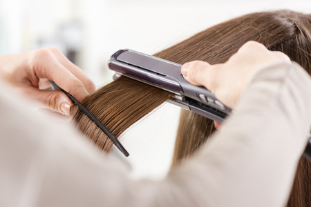 Hairdresser straightening long brown hair with hair irons.の写真素材