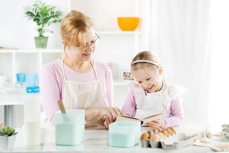 Beautiful happy grandmother and granddaughter reading cookery book in a kitchen. の写真素材