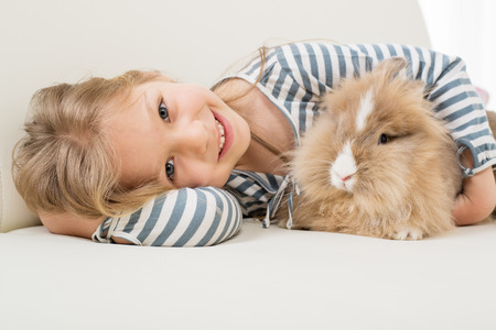 Little girl with her bunny laying on the sofa and huggingの写真素材