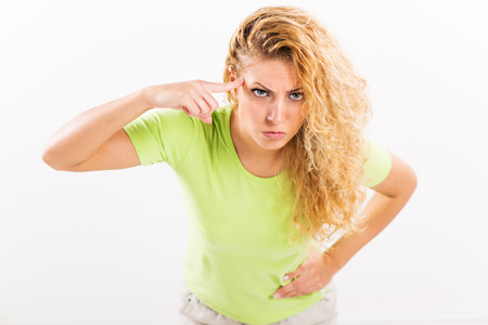 Angry young woman standing against a white background with a finger pressed against the head.の写真素材