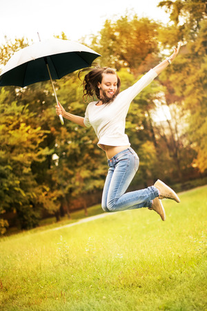 Young beautiful woman jumping in rainy autumn park with umbrella.の写真素材