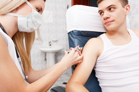 Young man getting flu shot needle vaccination in armの写真素材
