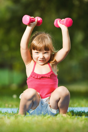Beautiful little girl with dumbbells in nature environmentの写真素材