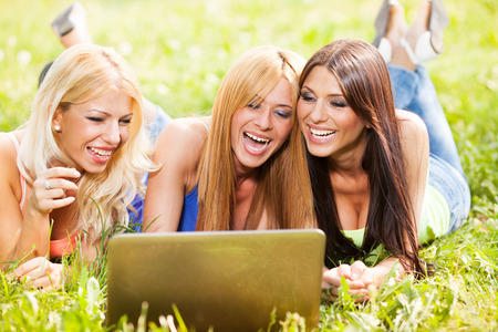 Beautiful girls with laptop at park surfing on the internetの写真素材