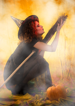 Young woman dressed like a witch. She is in dark clothing with broom.の写真素材