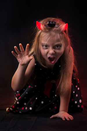 Little halloween witch in dark clothing with evil face wearing devil horns.の写真素材