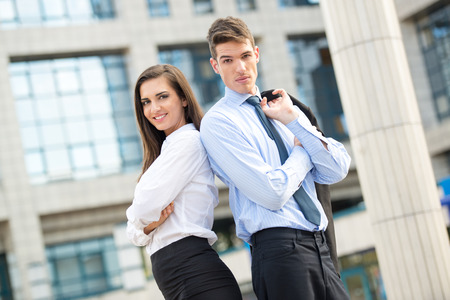 Young business couple standing in front of office building leaning back on each other.の写真素材