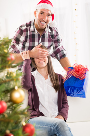 Young man gives his girlfriend a Christmas gift her hand over her eyes.の写真素材