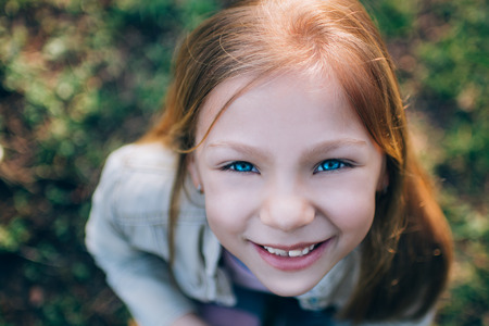 Close-up little girl's face with a smile and beautiful blue eyes looking at the camera. Photographed from aboveの写真素材