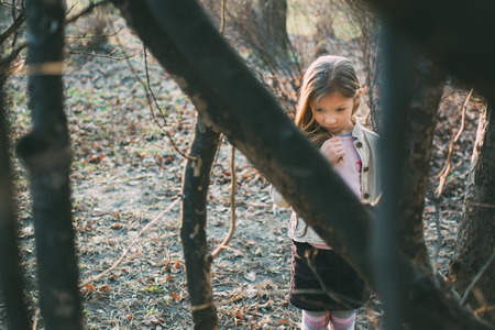 Little girl stands among the trees and with a sad expression on her face looking down.の写真素材