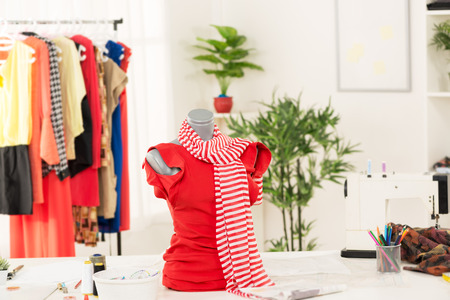 Dress on mannequin in fashion designer office. In addition to the mannequin on the table is sewing machine. In the background you can see hanging garments.の写真素材