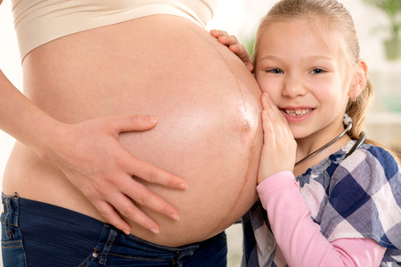 Close-up of a happy future sister listening to naked belly of his pregnant mother