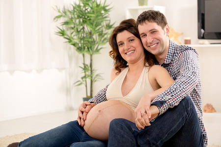 Portrait of a beautiful young couple cuddling the woman's pregnant belly. They smiling and looking at camera.の写真素材