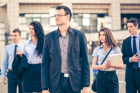 Young businessman, elegantly dressed, standing  with his team in front of office building. Everyone is looking to the side.の写真素材