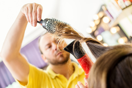 Man hairdresser drying long brown hair of a woman with hair dryer and round brush.の写真素材