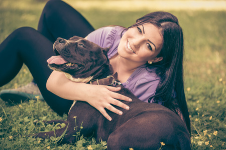 Beautiful young woman hugging her cute stafford terrier. They sitting on grass in the park and enjoyingの写真素材