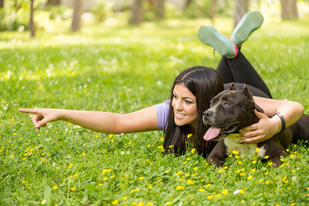Beautiful young woman with her cute stafford terrier lying on grass in the park.の写真素材