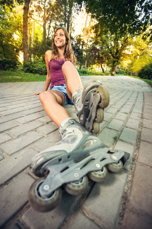 Beautiful girl roller sitting on track in the park and resting after roller skating. Focus on...