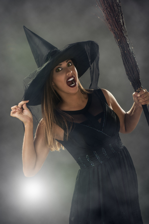 Young woman dressed like a witch in dark clothing and holding a broom.の写真素材
