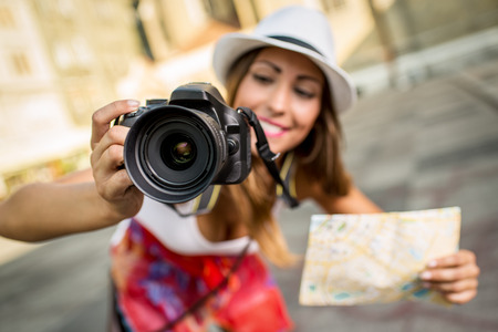 Close up of a beautiful young girl tourist holding map and photographing with digital camera. Selective focus. Focus on foreground.の写真素材