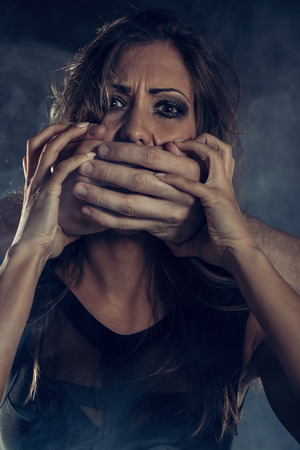 Young woman abuse victim with man's abuser hands on her mouth looking at cameraのeditorial素材